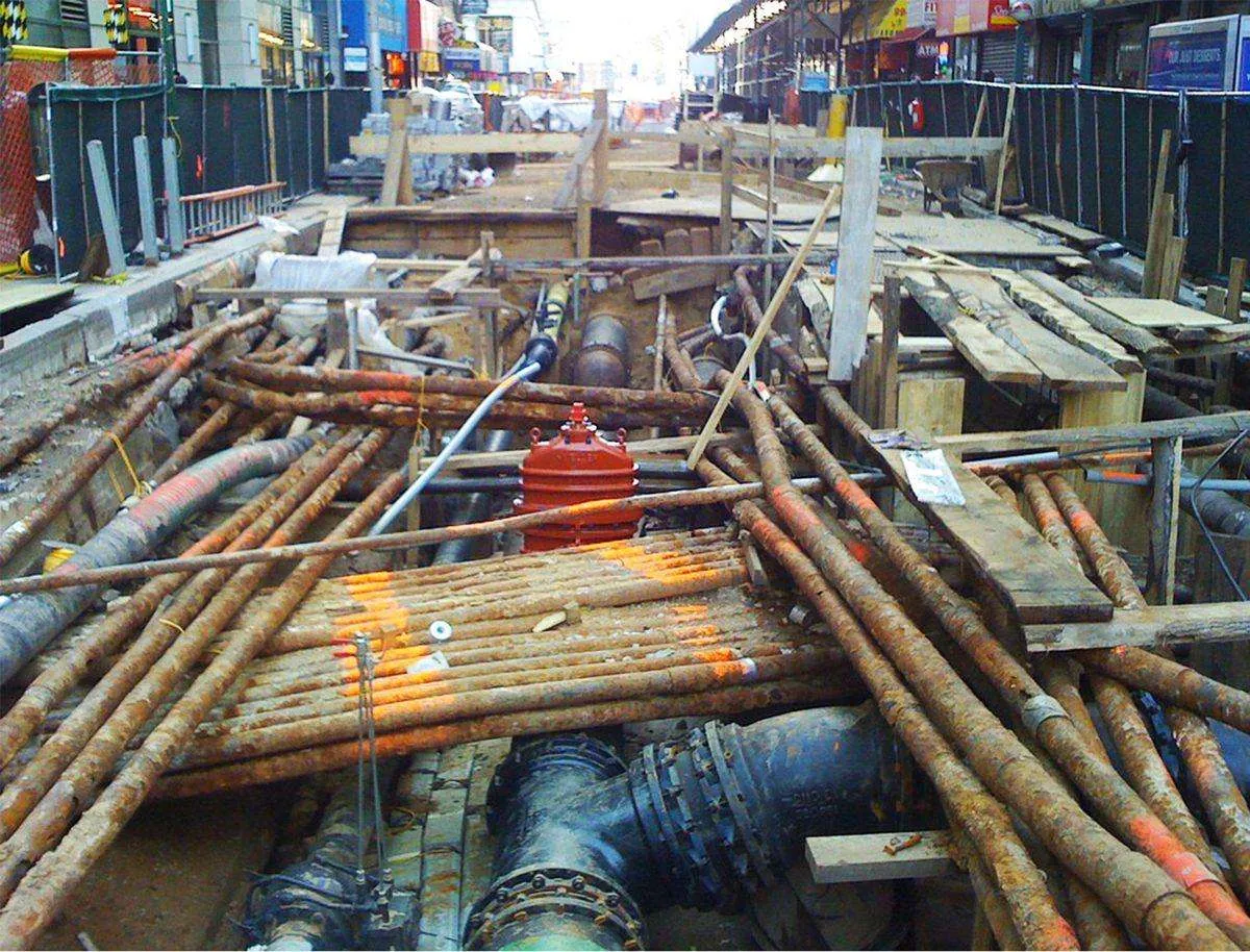 Exposed underground pipes and utility lines beneath a city street.