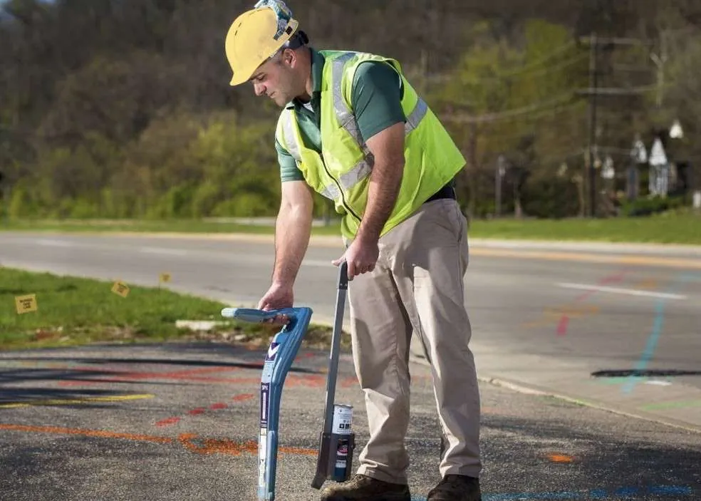A utility locator marks a buried line with spray paint beside a road